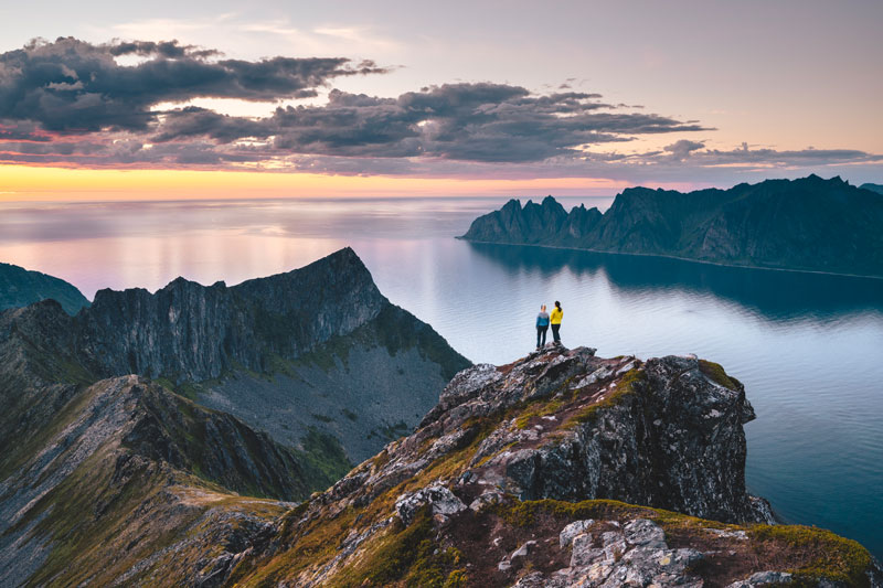 Två personer står på ett berg och ser på utsikten över havet
